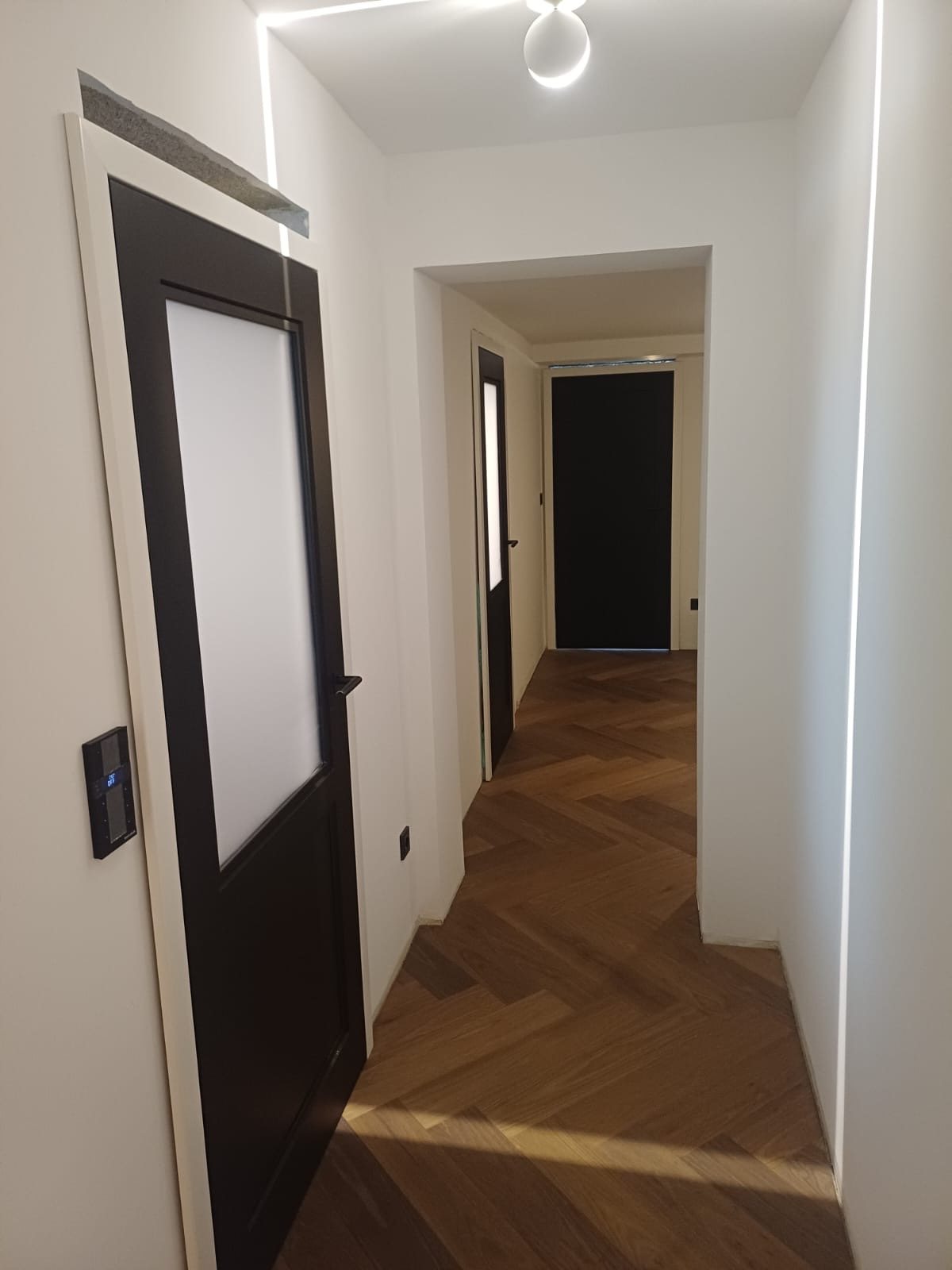 Schwarze Innentür mit Satinglas-Ausschnitt, Blick durch den Flur mit Fischgrätparkett