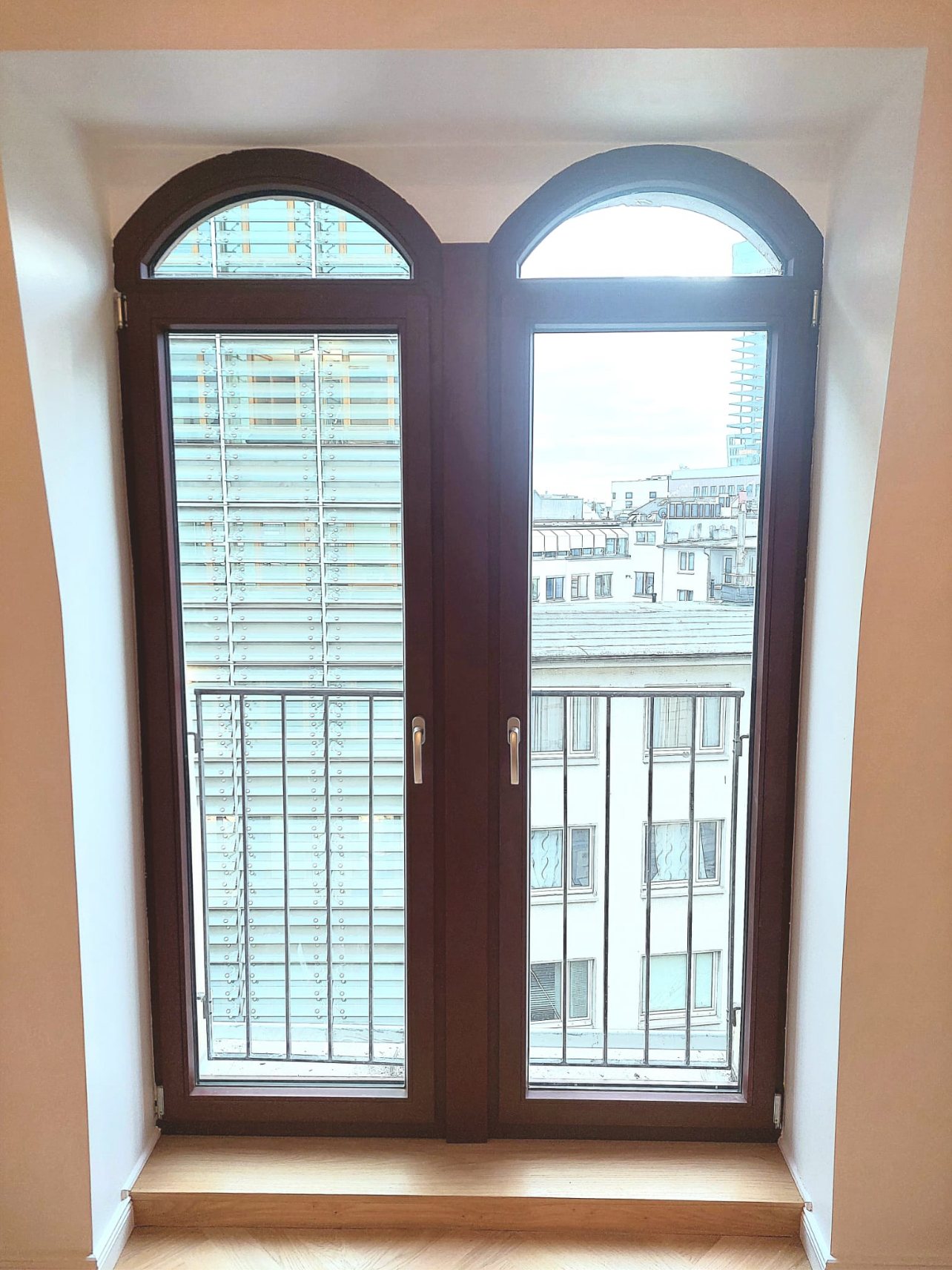 Zweiflügeliges Rundbogenfenster in dunklem Rotbraun, frontale Innenansicht mit Blick über die Dächer der Frankfurter Innenstadt
