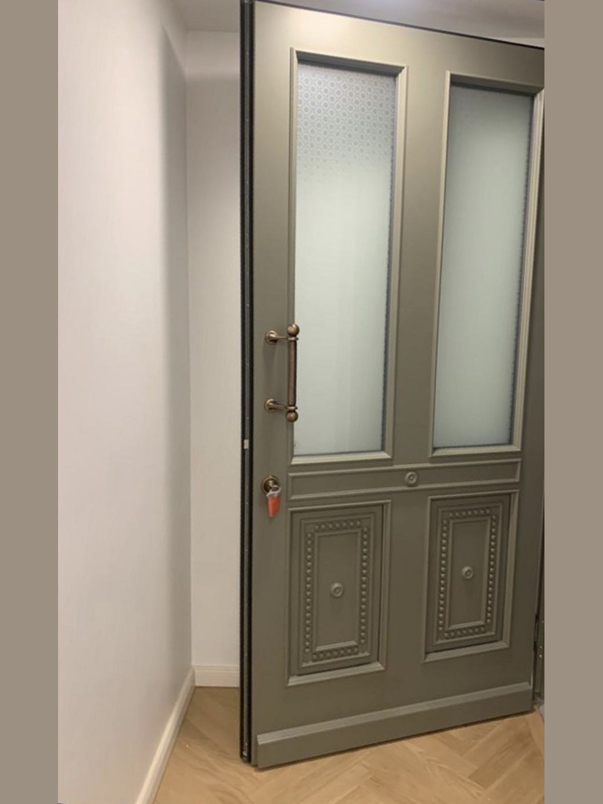 Wohnungseingangstür in Graugrün mit zwei Ornamentglas-Feldern, verzierten Kassetten und bronzefarbenem Stoßgriff
