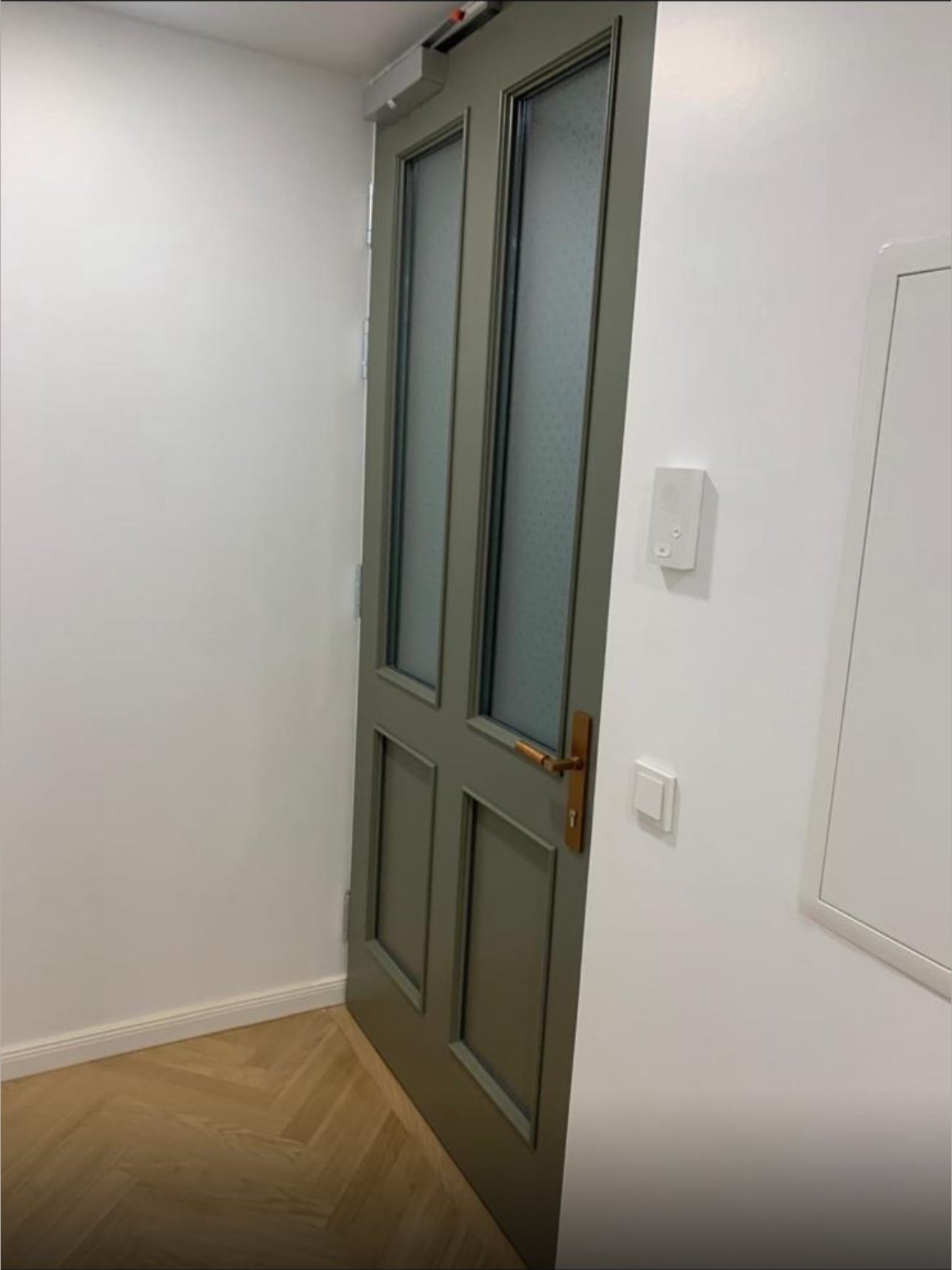 Eingebaute Wohnungseingangstür in Graugrün mit Ornamentglas, Türschließer und bronzefarbener Drückergarnitur