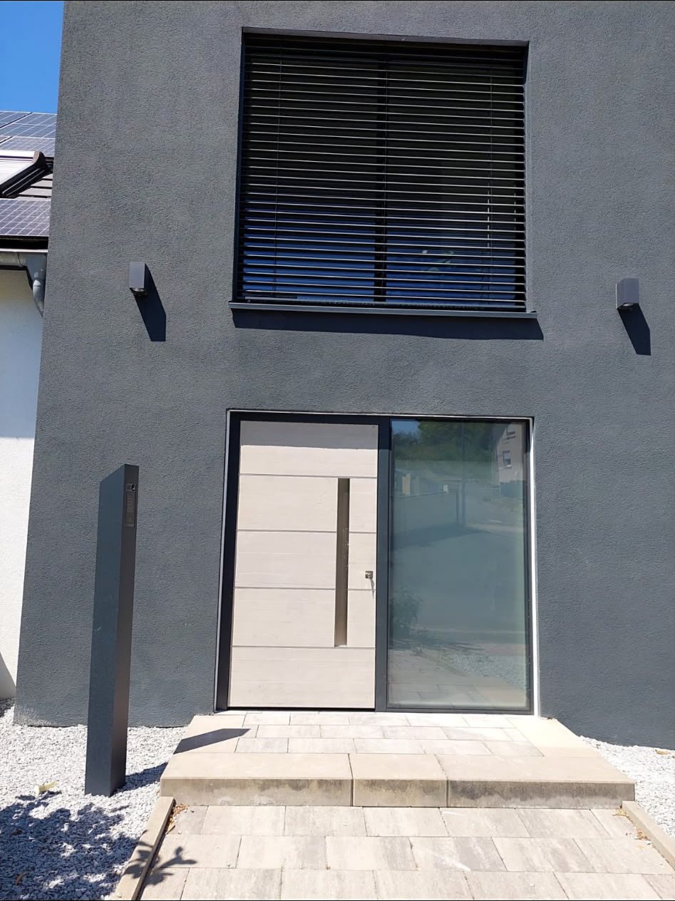 Hellgraue Aluminium-Haustür mit schmalem Glasseitenteil in einer anthrazitfarbenen Neubaufassade