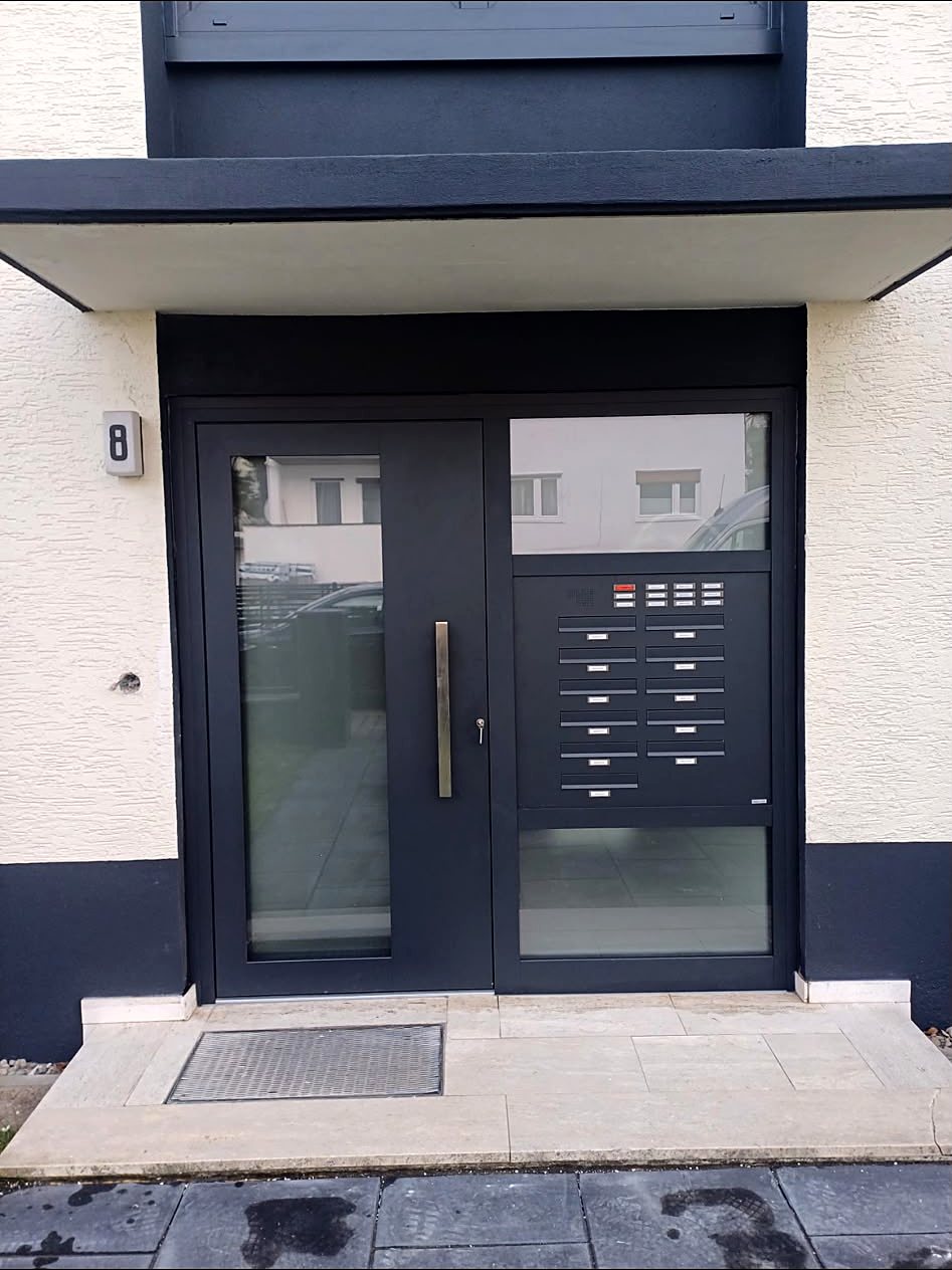 Anthrazitfarbene Haustür mit Glasseitenteil und eingebauter Briefkastenanlage an einem Mehrfamilienhaus